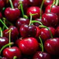 Adopt Au Feminin close-up of fresh, ripe red cherries with green stems, highlighting their smooth, glossy texture