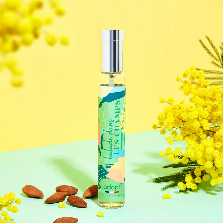 Adopt Balade Dans Les Champs perfume bottle with a green and yellow label, surrounded by yellow mimosa flowers and almonds