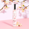 Adopt Fleur De Cerisier perfume bottle with cherry blossom design, displayed against a pink background with floral branches