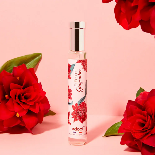 Adopt Fleur De Gingembre perfume bottle with a floral design, surrounded by red flowers on a pink background