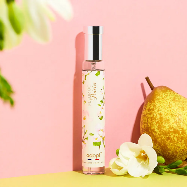 Adopt Fleur De Poirier fragrance bottle with a floral design, displayed on a pink and yellow background with a pear and