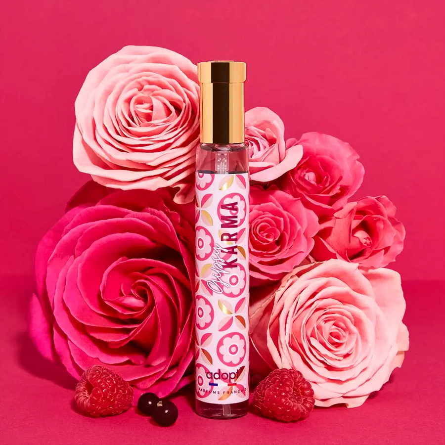 Adopt Gipsy Karma perfume bottle with a gold cap and pink floral pattern, surrounded by pink roses and raspberries
