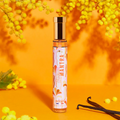 Adopt Hippie Mantra perfume bottle with a gold cap and a colorful label, surrounded by yellow mimosa flowers and vanilla pods