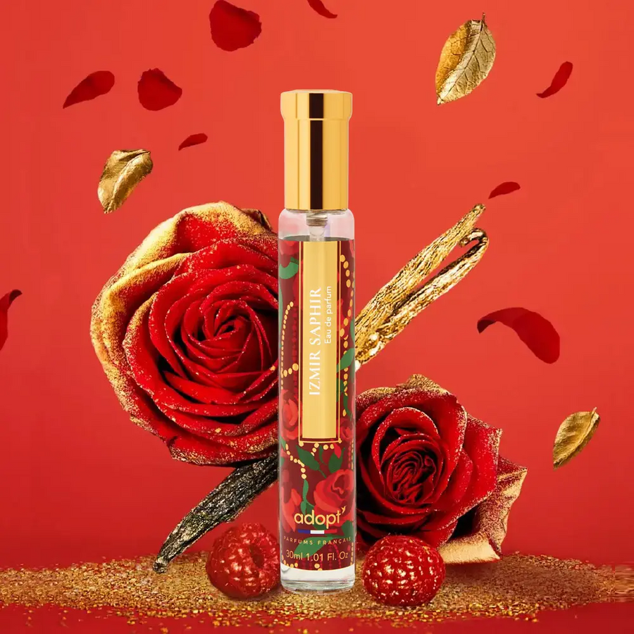 Adopt Izmir Saphir Eau de Parfum bottle with a gold cap, surrounded by red roses, gold leaves, and raspberries