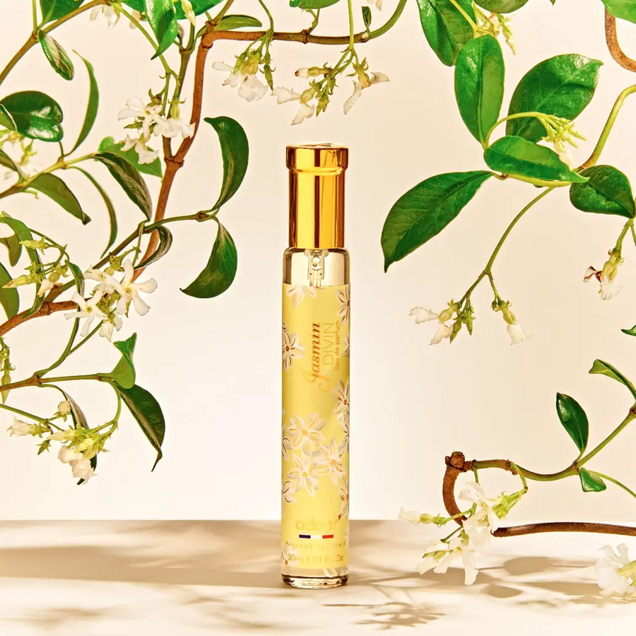 Adopt Jasmin Divin Eau de Parfum in a yellow bottle with white floral patterns, surrounded by jasmine vines and flowers