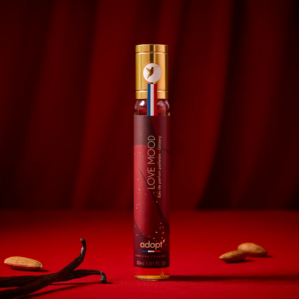 Adopt Love Mood Eau de Parfum Pailletee Glittery, 30ml bottle, with vanilla pods and almonds on a red background