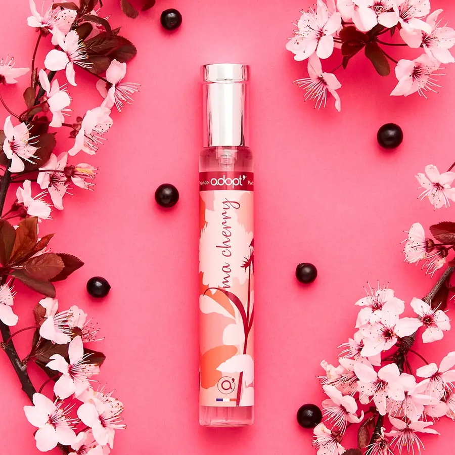 Adopt Ma Cherry perfume bottle with a cherry blossom design, surrounded by pink flowers and dark berries on a pink background