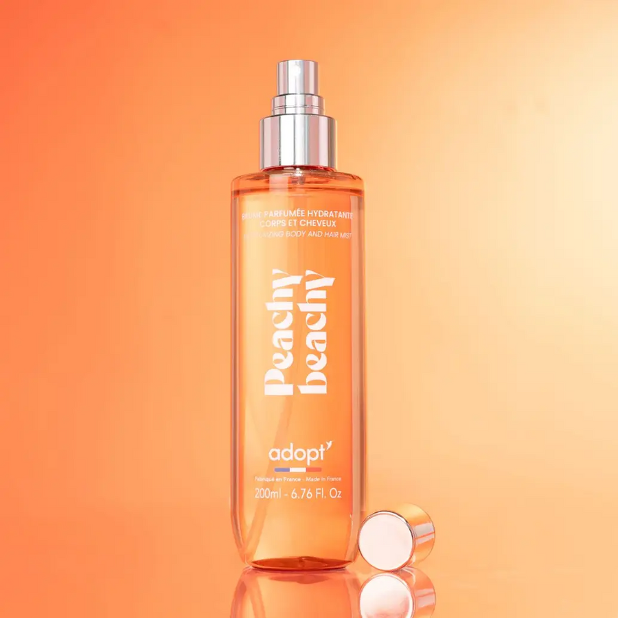 Adopt Peachy Beachy Body & Hair Mist in a clear bottle with a silver spray top and a rose gold cap next to it,