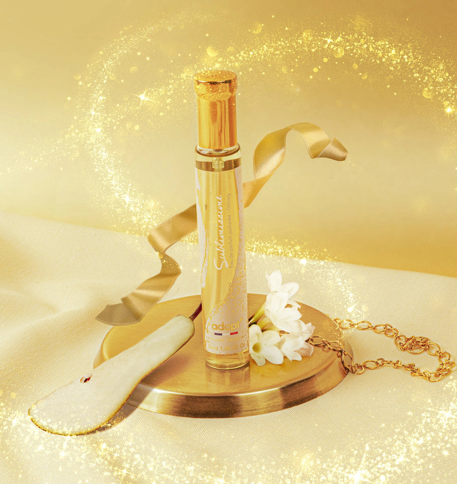 Adopt Sublimissime glittery eau de parfum with a golden ribbon, white flowers, and a pear slice on a gold tray