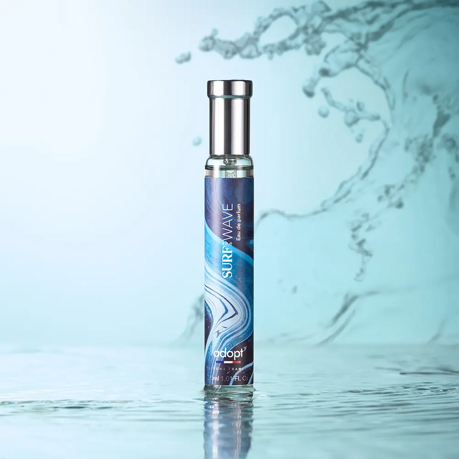 Adopt Surf The Wave Eau de Parfum in a sleek bottle with a blue and white wave design, standing on a reflective water surface